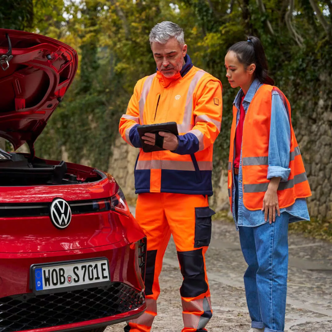 Un agente de servicio junto a un coche con una tablet al lado de un Volkswagen